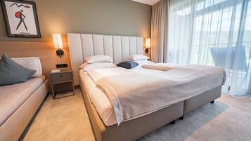 Habitación de hotel con una cama grande, una mesita de noche, un sofá y una lámpara de pared.