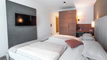 Une chambre d’hôtel avec deux lits, un téléviseur à écran plat fixé au mur, une armoire en bois et une table de chevet avec une lampe.