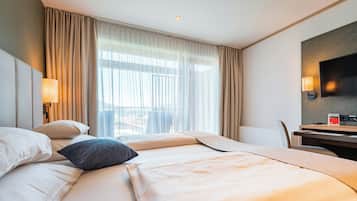 Une chambre d’hôtel avec un lit, un bureau, une chaise, une télévision et une fenêtre avec des rideaux.