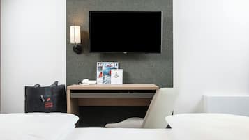 Ein Hotelzimmer mit einem Bett, einem Schreibtisch mit Flachbildfernseher, einer Wandlampe und einer Tasche auf dem Boden.