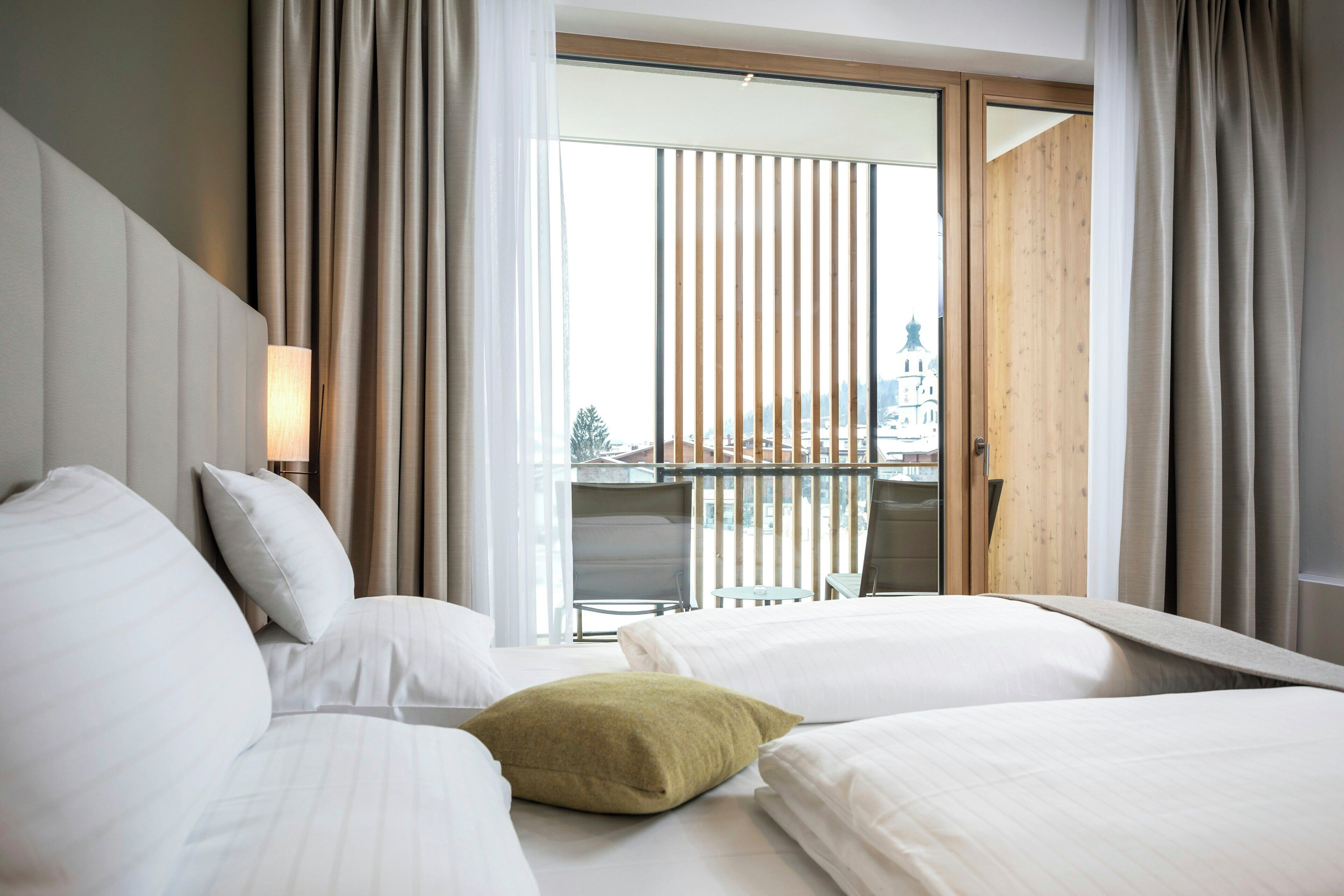 Una habitación de hotel con una cama, una mesita de noche, una lámpara y vistas a un balcón con una mesa y sillas.