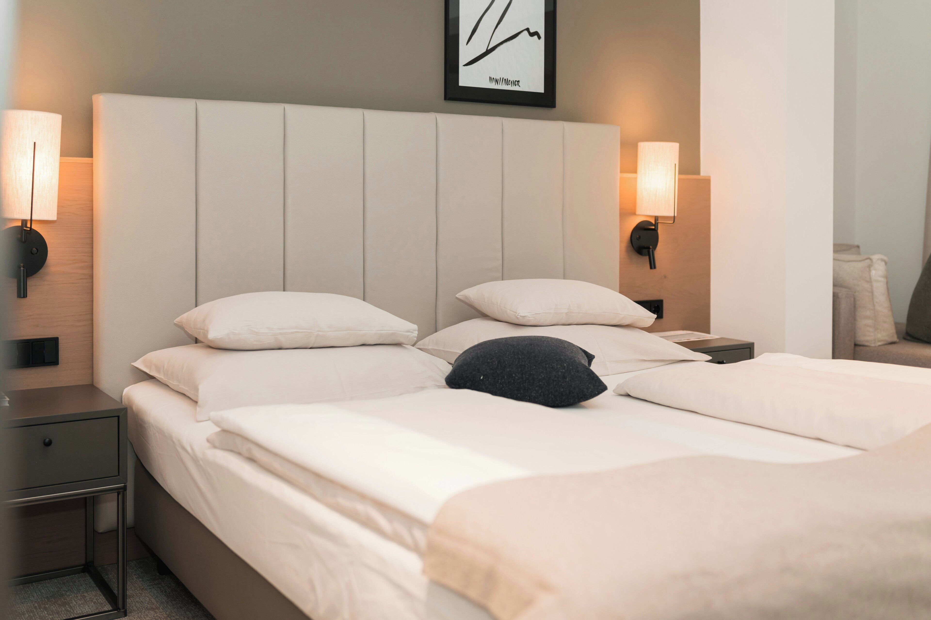 Habitació d'hotel amb un llit gran, dues taules de nit, una tauleta i una làmpada penjada a la paret, a més d'un quadre al capçal del llit.