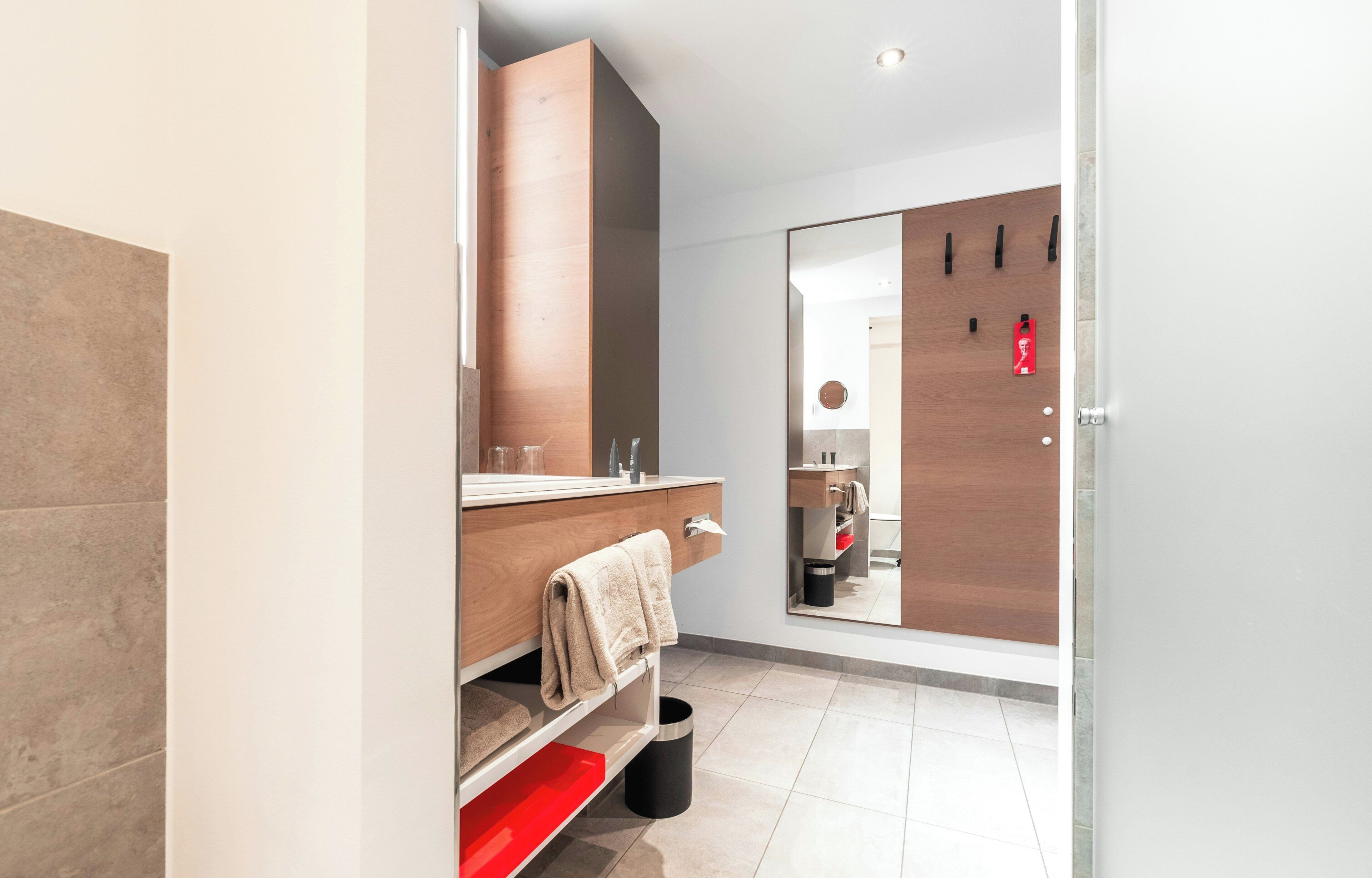 Un baño moderno con tocador de madera, un espejo y un perchero rojo.