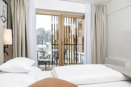 Habitación de hotel con cama, mesita de noche, lámpara y vistas a un balcón con mesa y sillas.