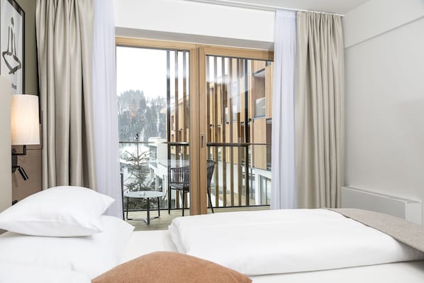Ein Hotelzimmer mit Bett, Nachttisch, Lampe und Blick auf einen Balkon mit Tisch und Stühlen.