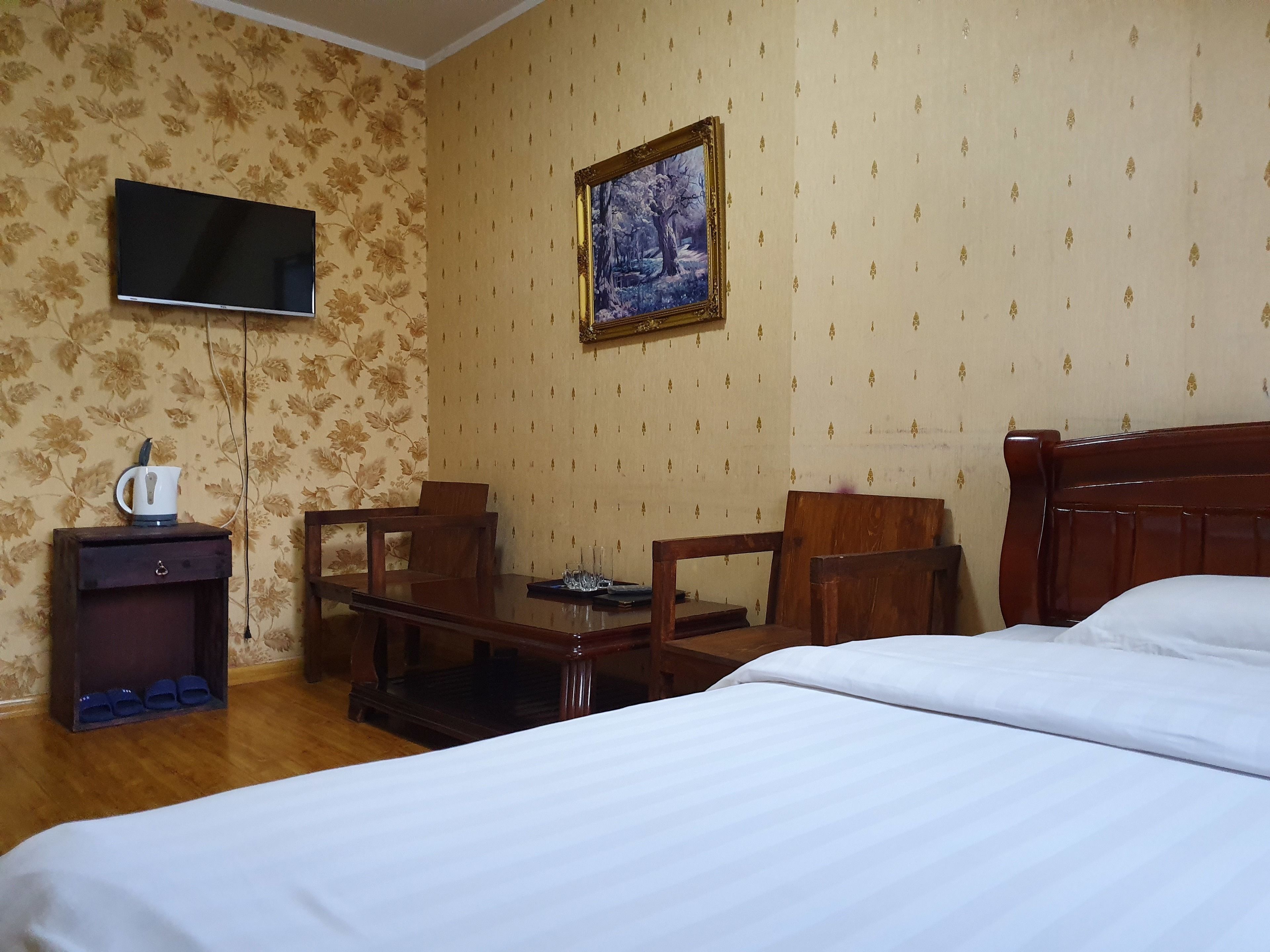 A hotel room with a bed, a desk with a chair, a television, and a painting on the wall.