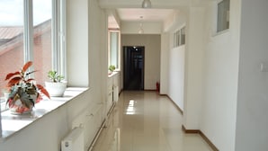 A long, narrow hallway with white walls and a tiled floor. There are potted plants on a window sill and a radiator along the wall. - Land Hotel (Ulaanbaatar)