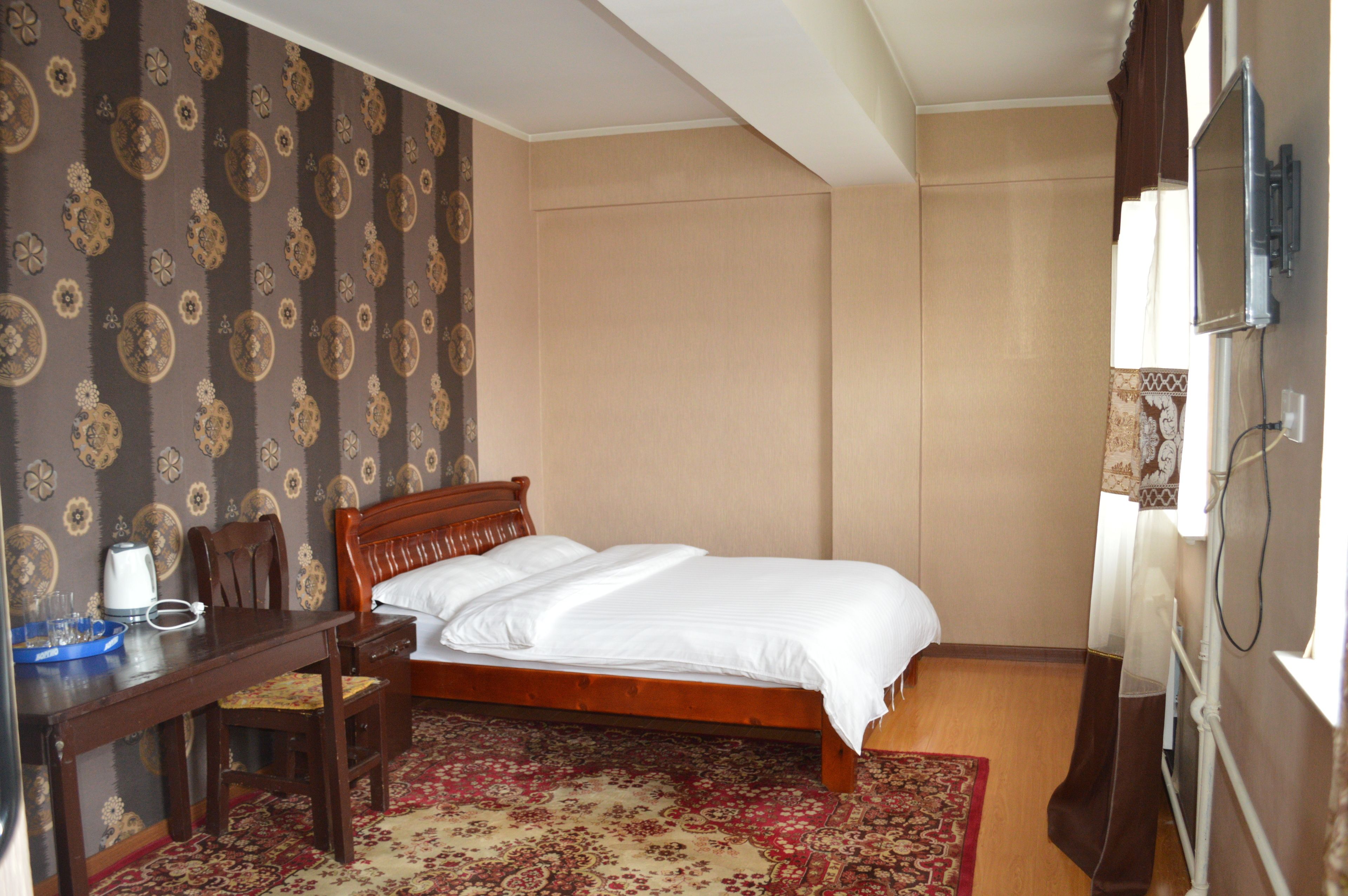 Ein ordentlich eingerichtetes Hotelzimmer mit einem Bett, einem Schreibtisch mit Stuhl, einem Fernseher und einem gemusterten Teppich.