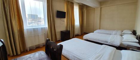 A hotel room with two single beds, a wooden desk, a chair, a television, and a window with curtains.