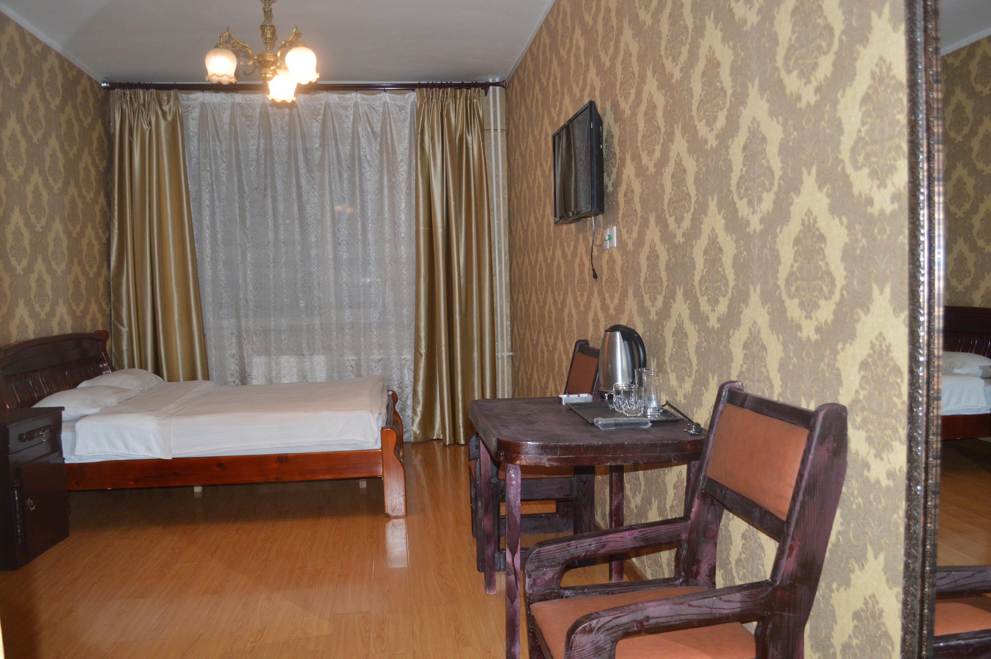 A hotel room with a bed, a table with a kettle, and a chair.