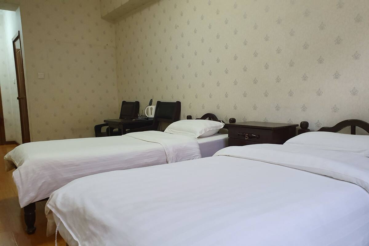 Quarto com duas camas de solteiro, uma pequena escrivaninha com cadeira e mesa de cabeceira.