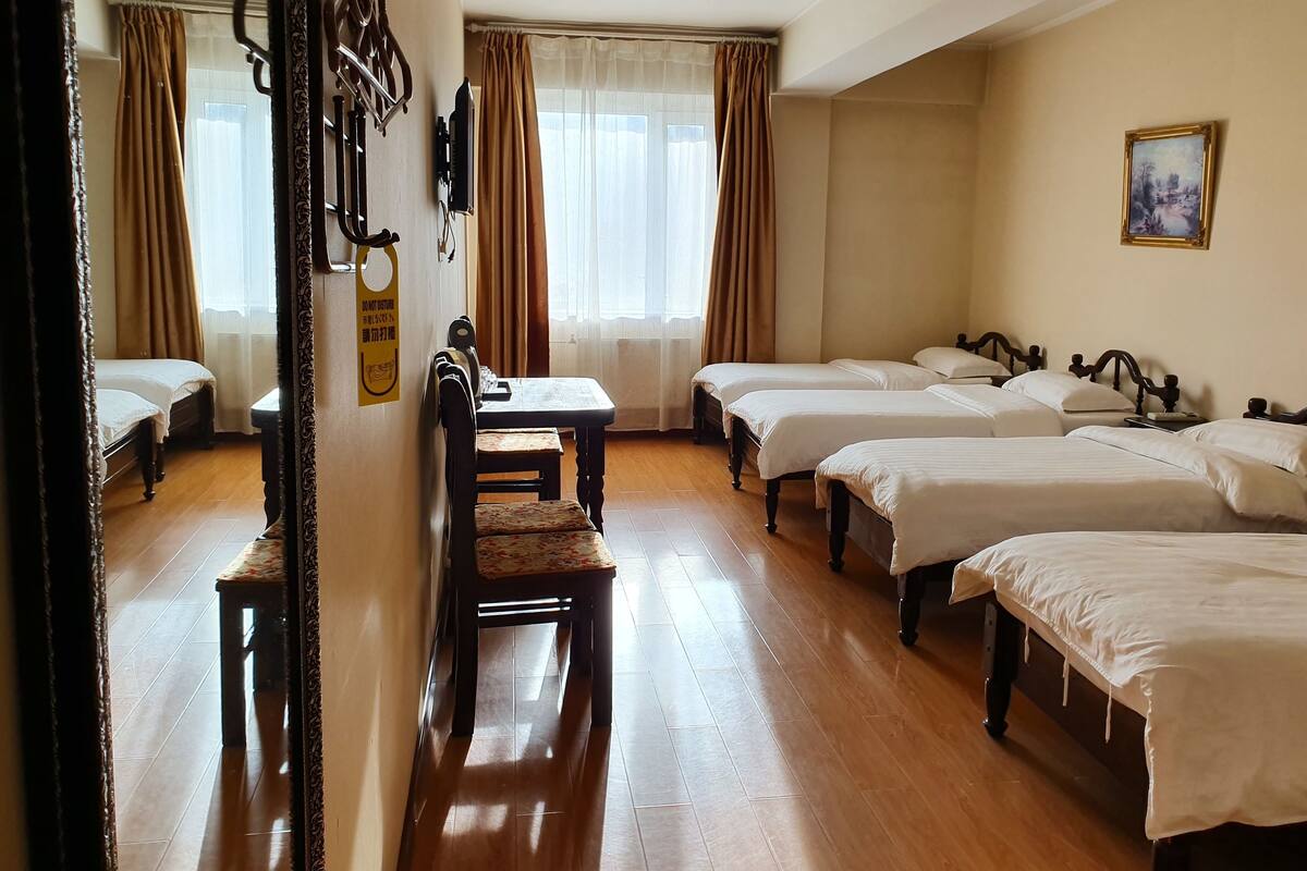 Quarto de hotel com quatro camas individuais, uma mesa de jantar de madeira, uma cadeira e uma pequena escrivaninha.