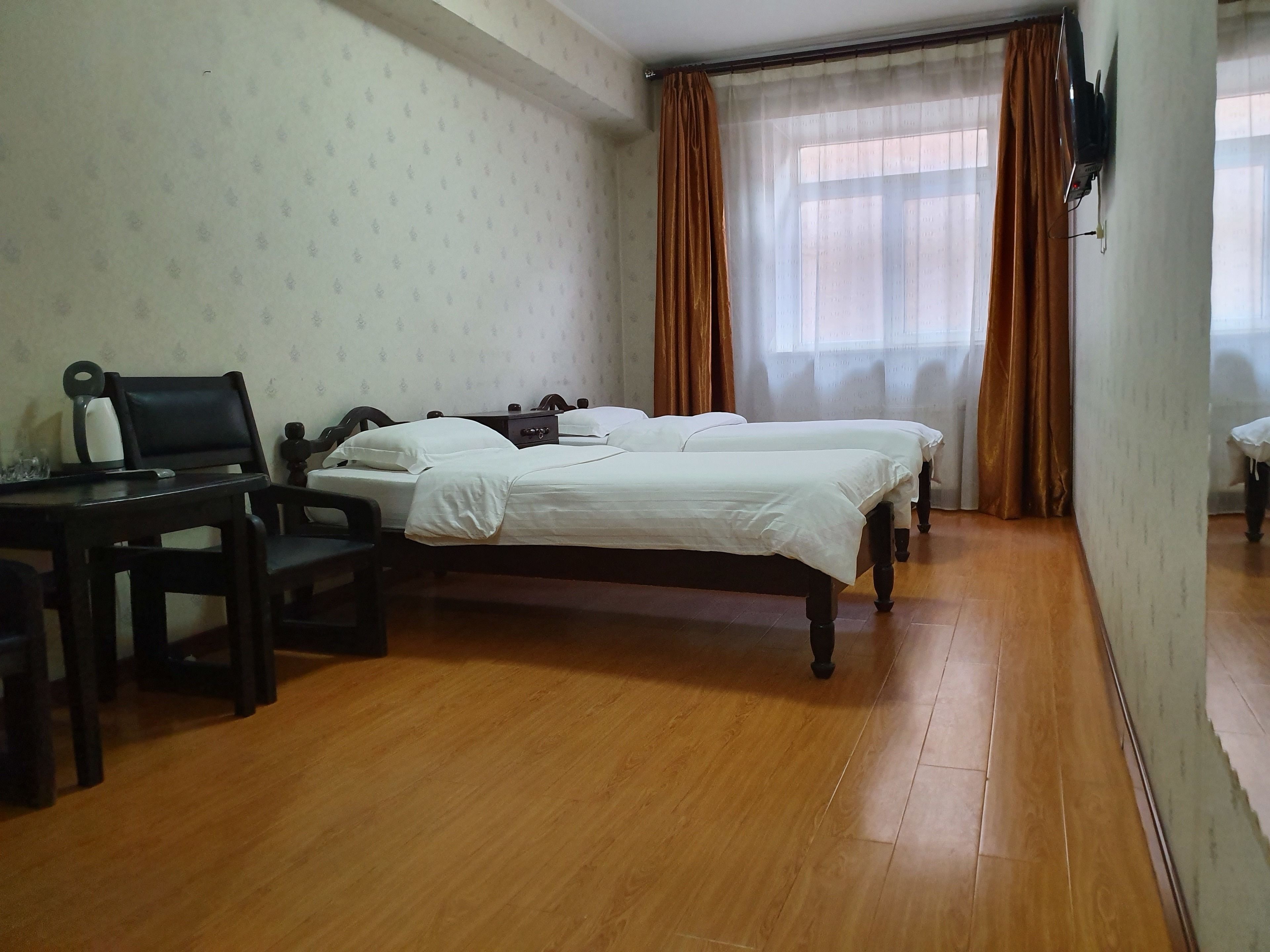 Une chambre avec deux lits simples, un bureau en bois avec une chaise, une petite table et un téléviseur fixé au mur.