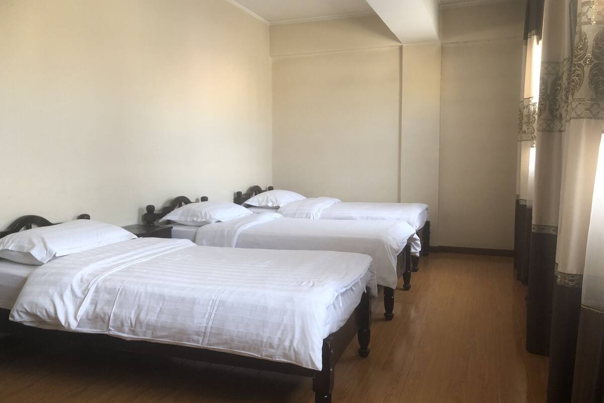 Quarto de hotel com três camas de solteiro, cabeceiras de madeira e piso de madeira.