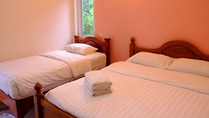 Una habitación con dos camas de madera, cada una con ropa de cama blanca y una toalla doblada sobre una de ellas.