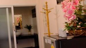 Una habitación con puerta de vidrio corredera que da a un baño, un refrigerador negro, aire acondicionado instalado en la pared, un televisor de montaje en pared y una orquídea ornamental.
