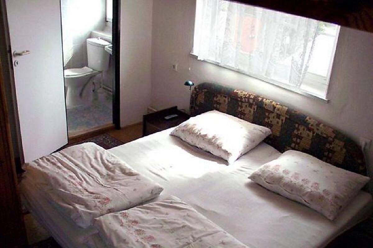 A single bed with floral bedding, a window with sheer curtains, and a view of a bathroom.