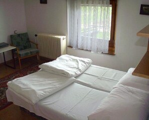 A room with two single beds, a chair, a radiator, and a window with sheer curtains. - Penzión Závada (Nova Lesna)