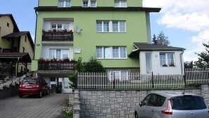A two-story building with a green facade, multiple windows, and a balcony with red flowers. - Penzión Závada (Nova Lesna)