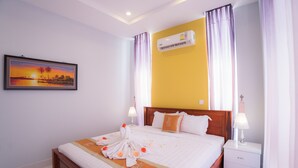 A neatly made bed with a towel and rose arrangement, a bedside table with a lamp, and an air conditioning unit on the wall. - Monorom Apartment Boeung Kang Keng 1 (Phnom Penh)
