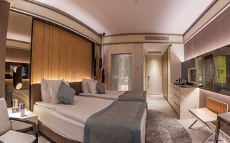 A hotel room with a bed, bedside tables, a desk, a chair, a TV, and a wardrobe.