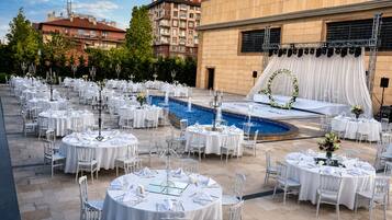 An outdoor wedding venue with round tables, chairs, a pool, and a stage with drapes.