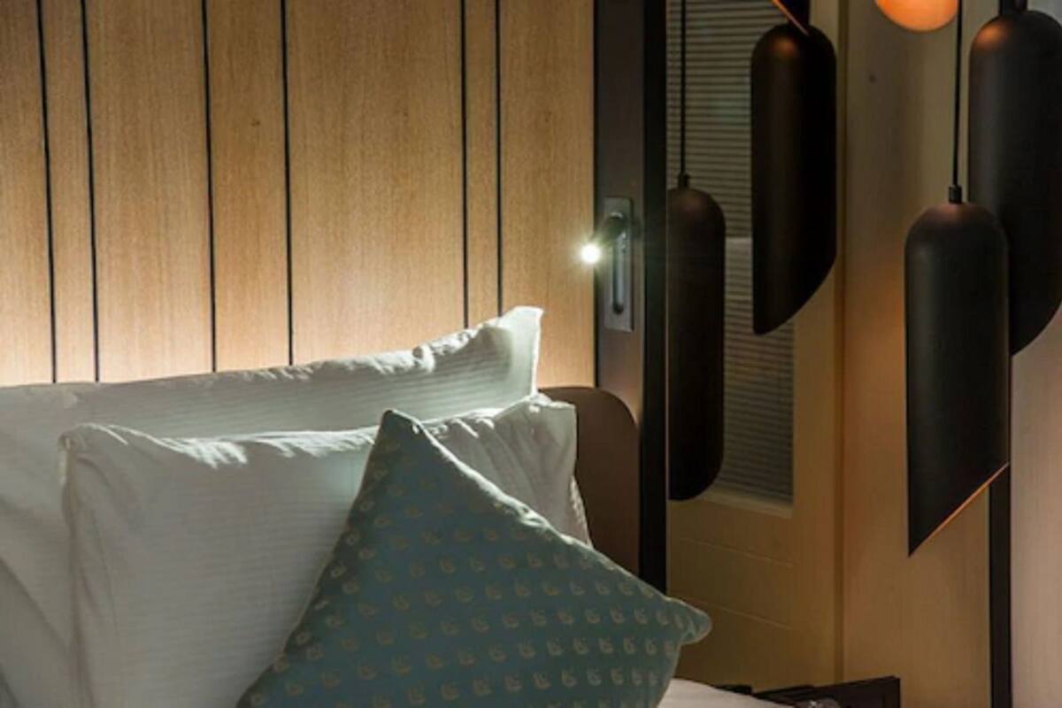 Un lit avec des oreillers, un mur en bois et des lampes suspendues.