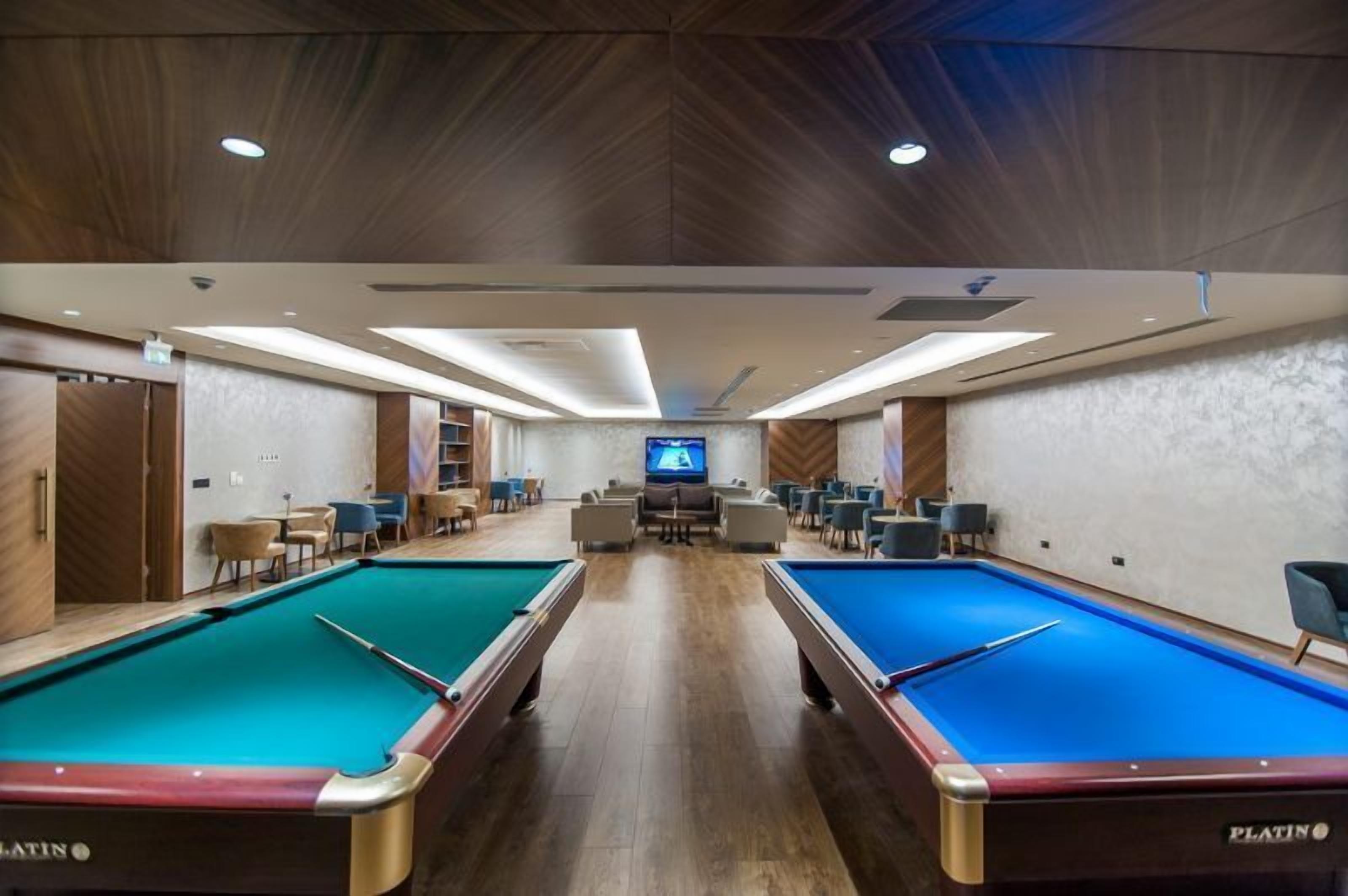 A pool area with two pools, chairs, a television, and a wooden ceiling.