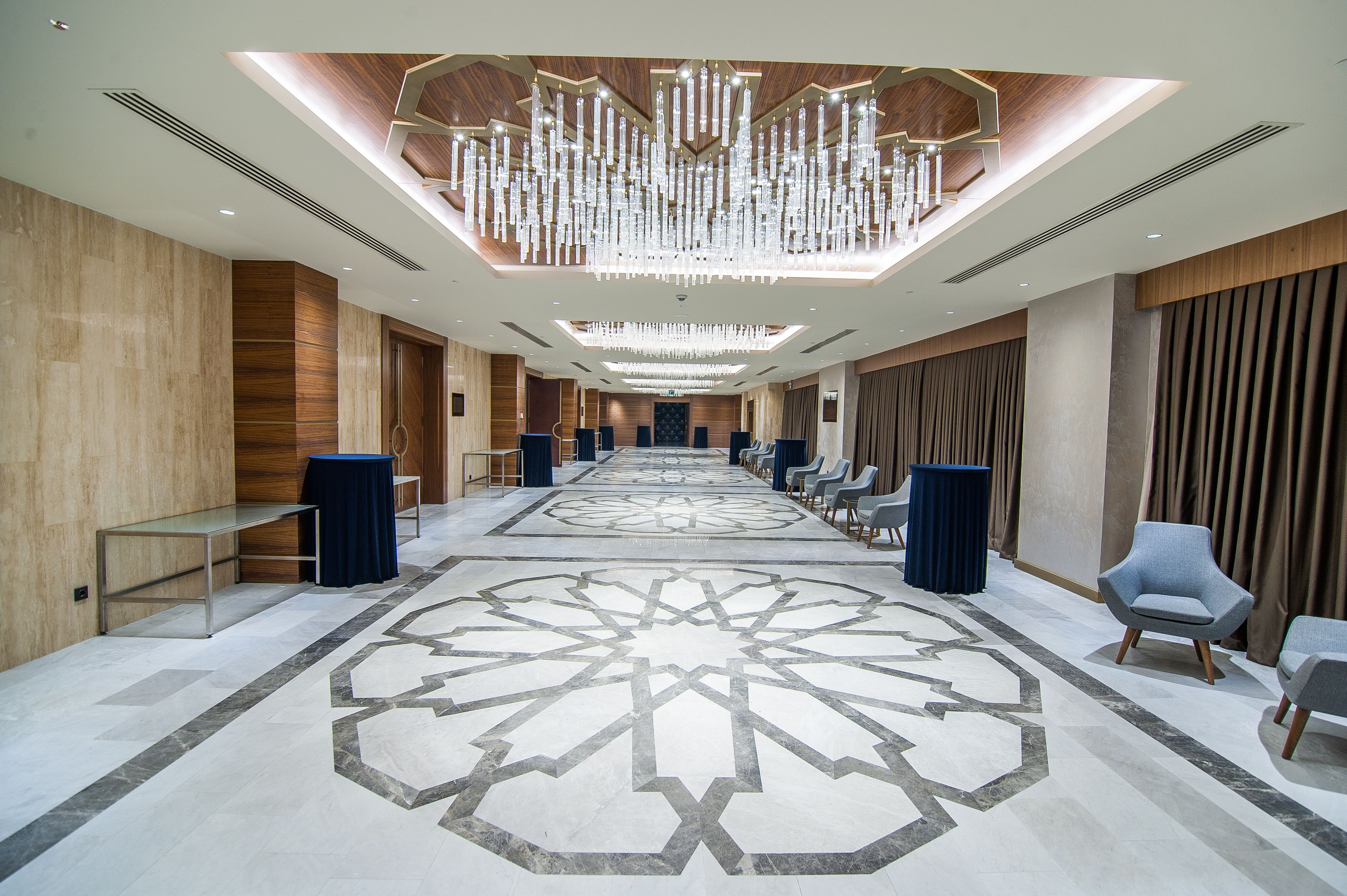 A spacious hotel lobby with a long reception desk, seating area, and a large chandelier.