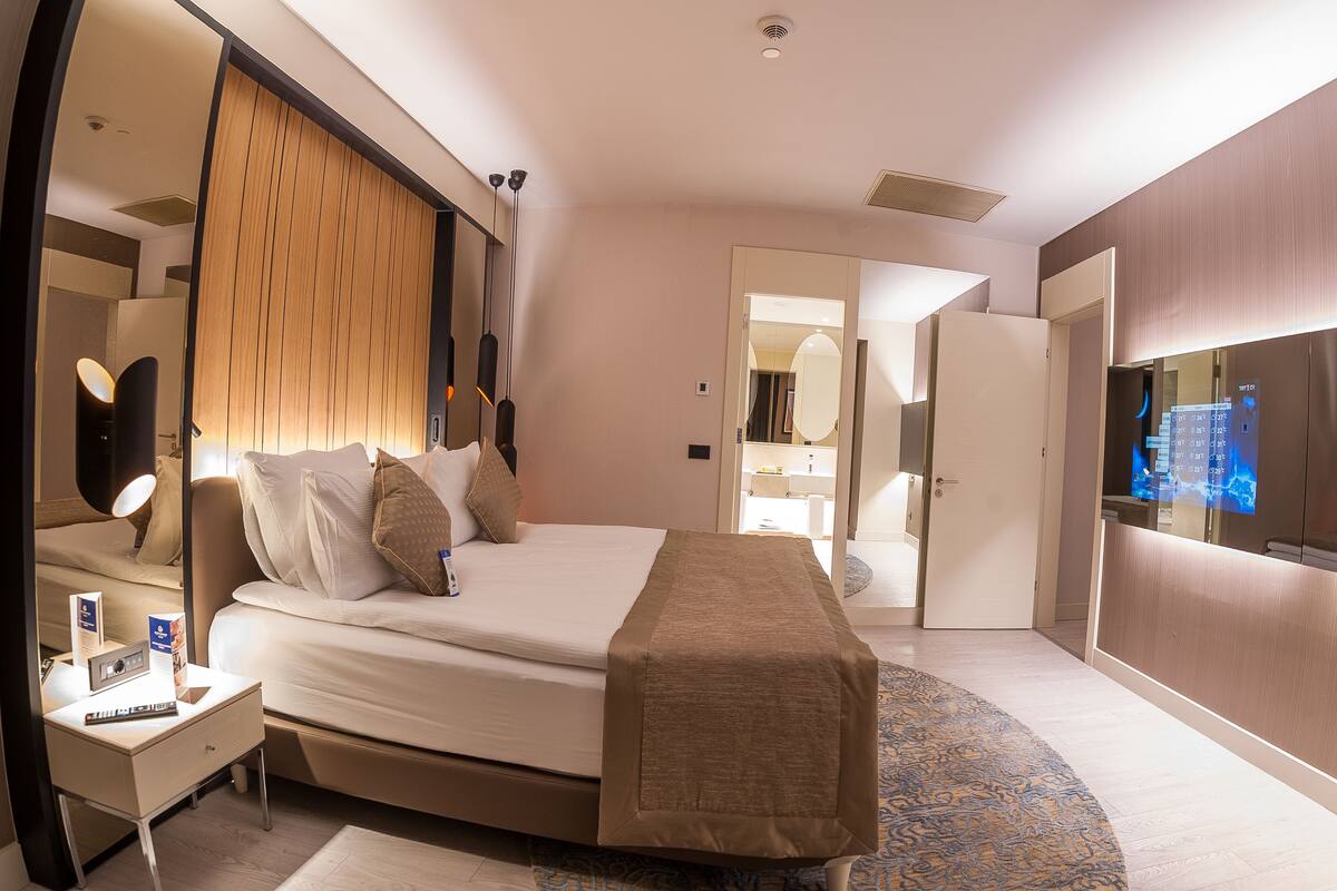 Une chambre d’hôtel moderne avec un grand lit, des tables de chevet, un miroir et un téléviseur.