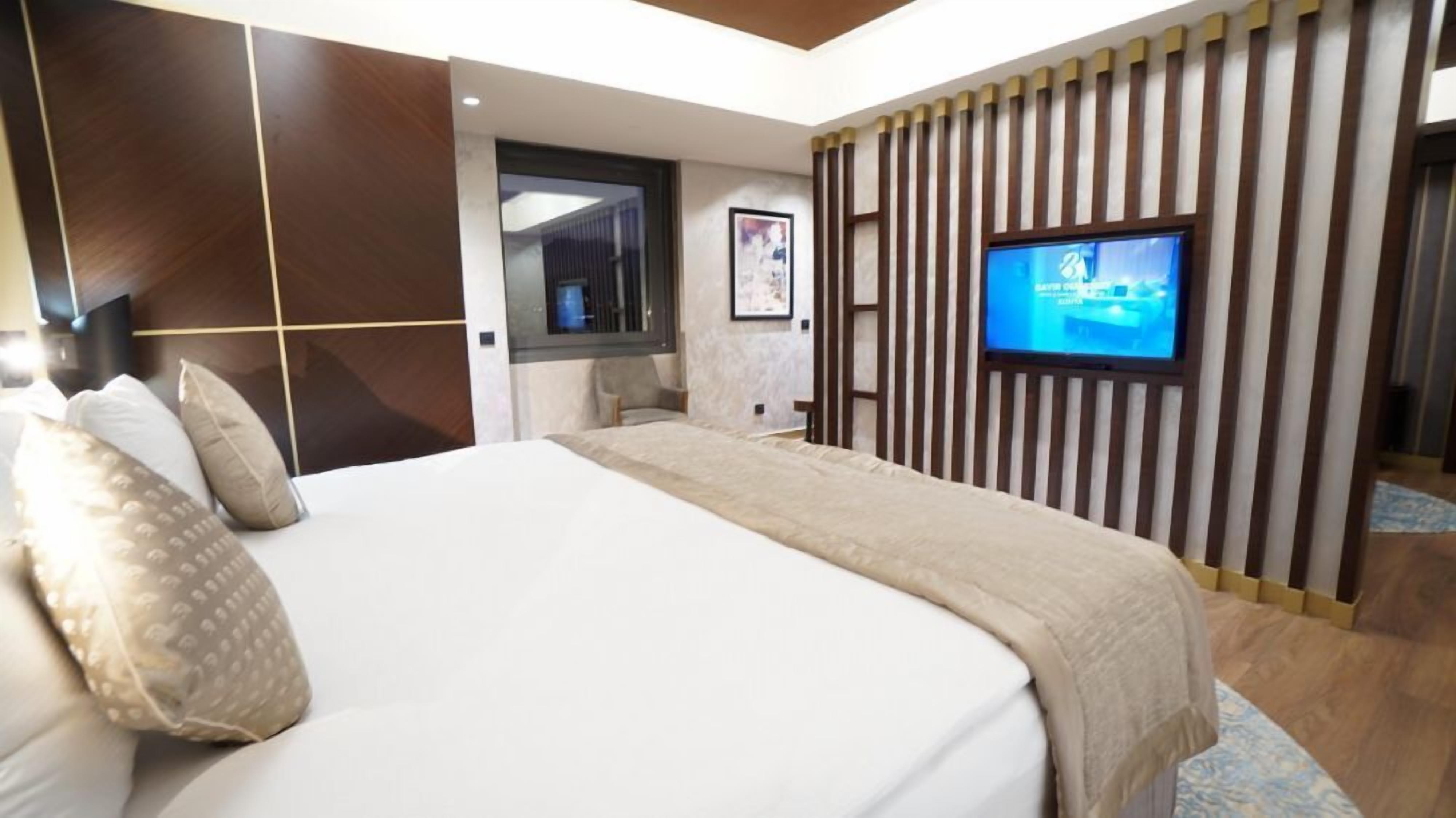 Ein modernes Hotelzimmer mit einem großen Bett, einem Fernseher, einer kleinen Sitzecke und einer dekorativen Wandverkleidung.