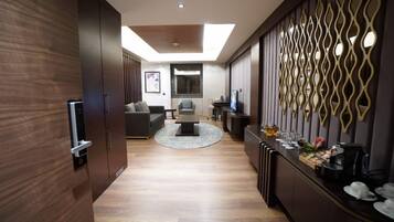 A modern living room with a sofa, coffee table, and a TV. There is a decorative wall with a geometric pattern and a small bar area with glasses and a coffee machine.