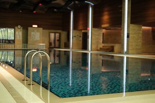 An indoor swimming pool with clear water, metal railings, and a tiled floor.