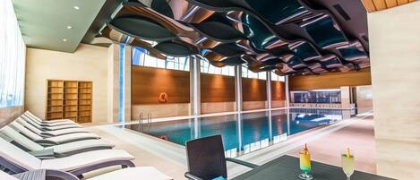 A modern indoor pool area with lounge chairs and a table with drinks.