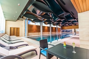 Un área de piscina interior moderna con sillones reclinables y una mesa con bebidas.