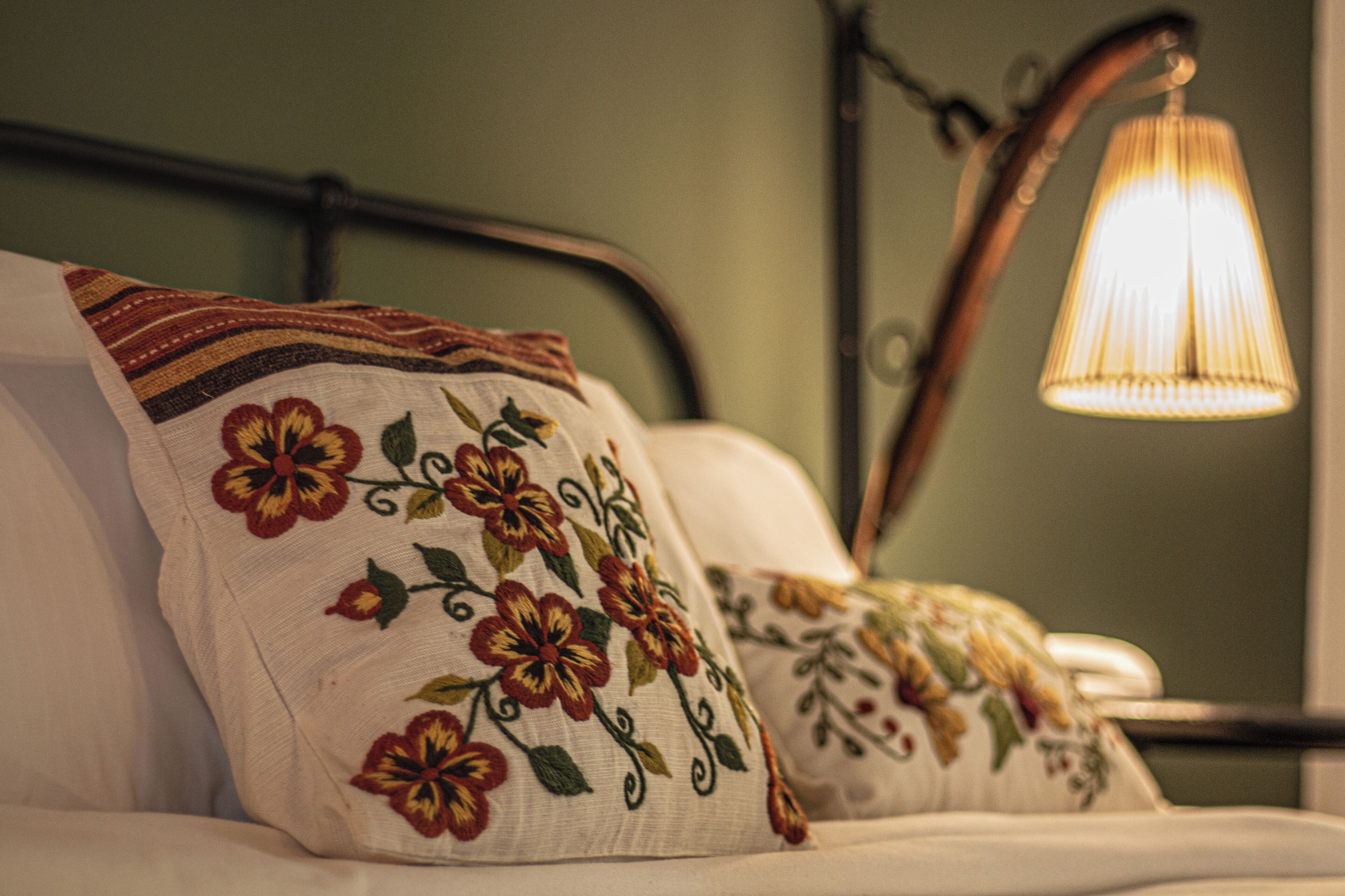 Una cama con almohadillas florales y una lámpara de noche.