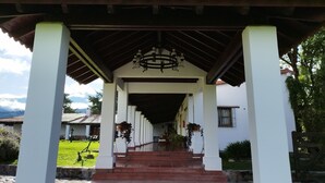 A covered walkway leading to a building with a tiled roof and a cross at the top.