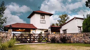 A two-story building with a red-tiled roof, a stone wall, and a sign indicating it is a hotel. - Finca Las Margaritas (Chicoana)