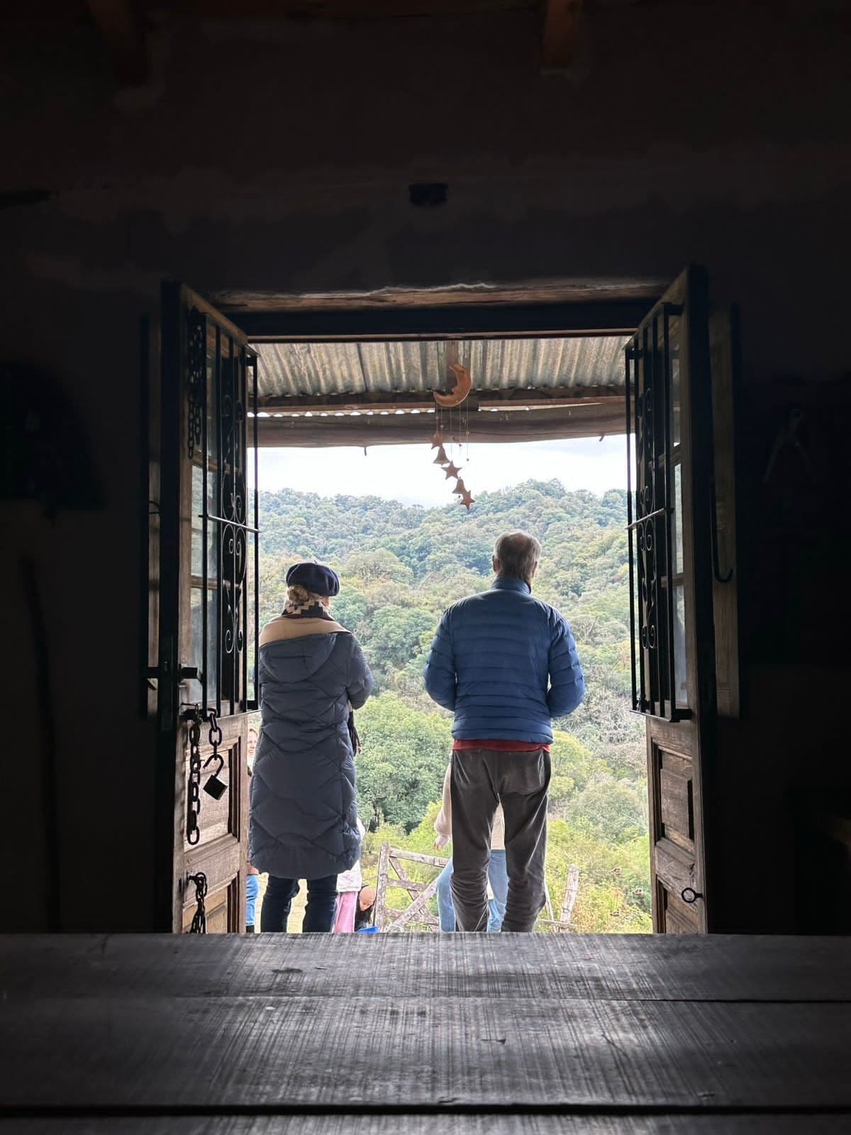 Quarto com porta aberta que dá para uma varanda com vista para uma encosta arborizada.