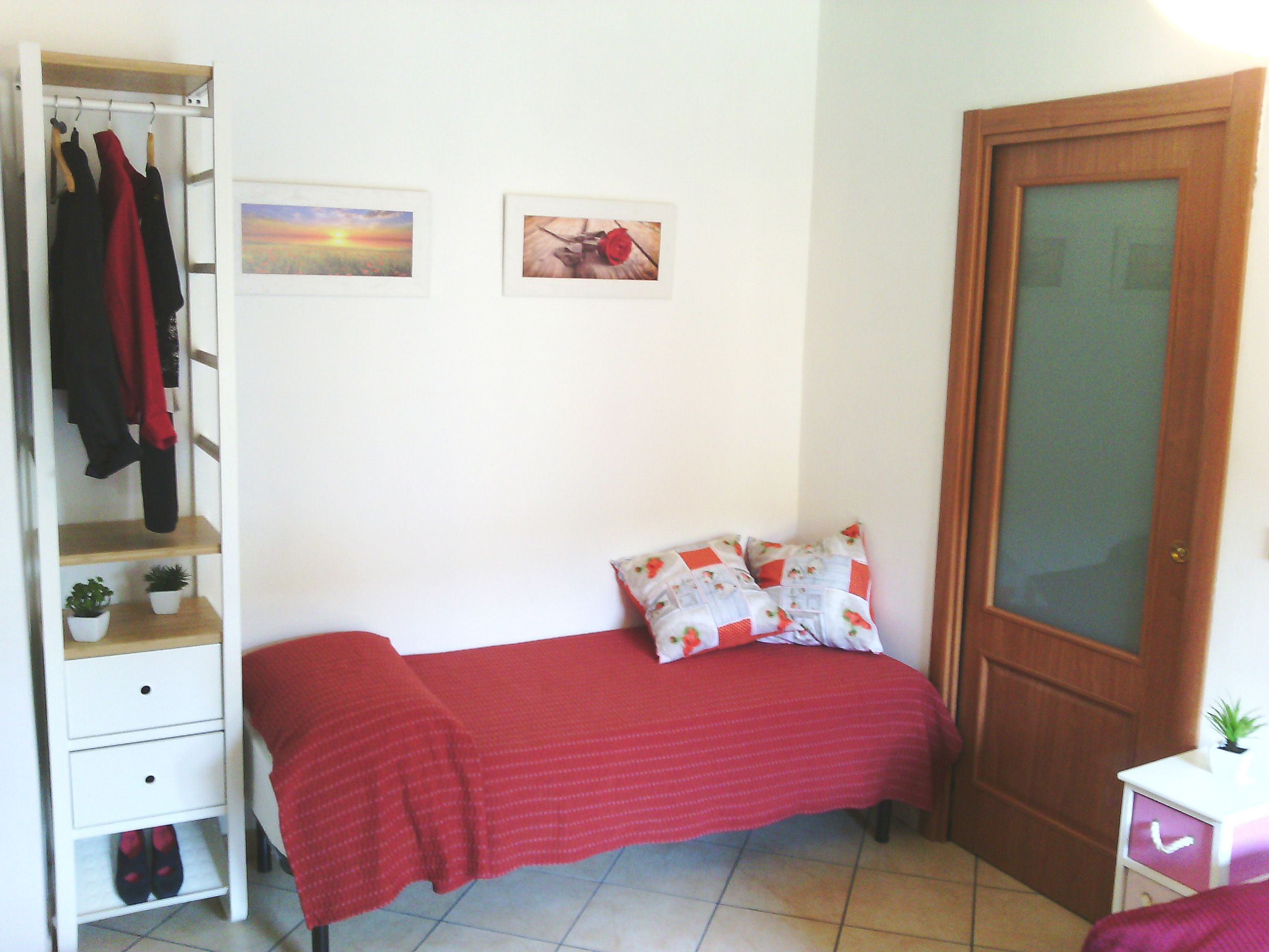 Un dormitorio con cama, un armario, una puerta y dos estantes pequeños con plantas.