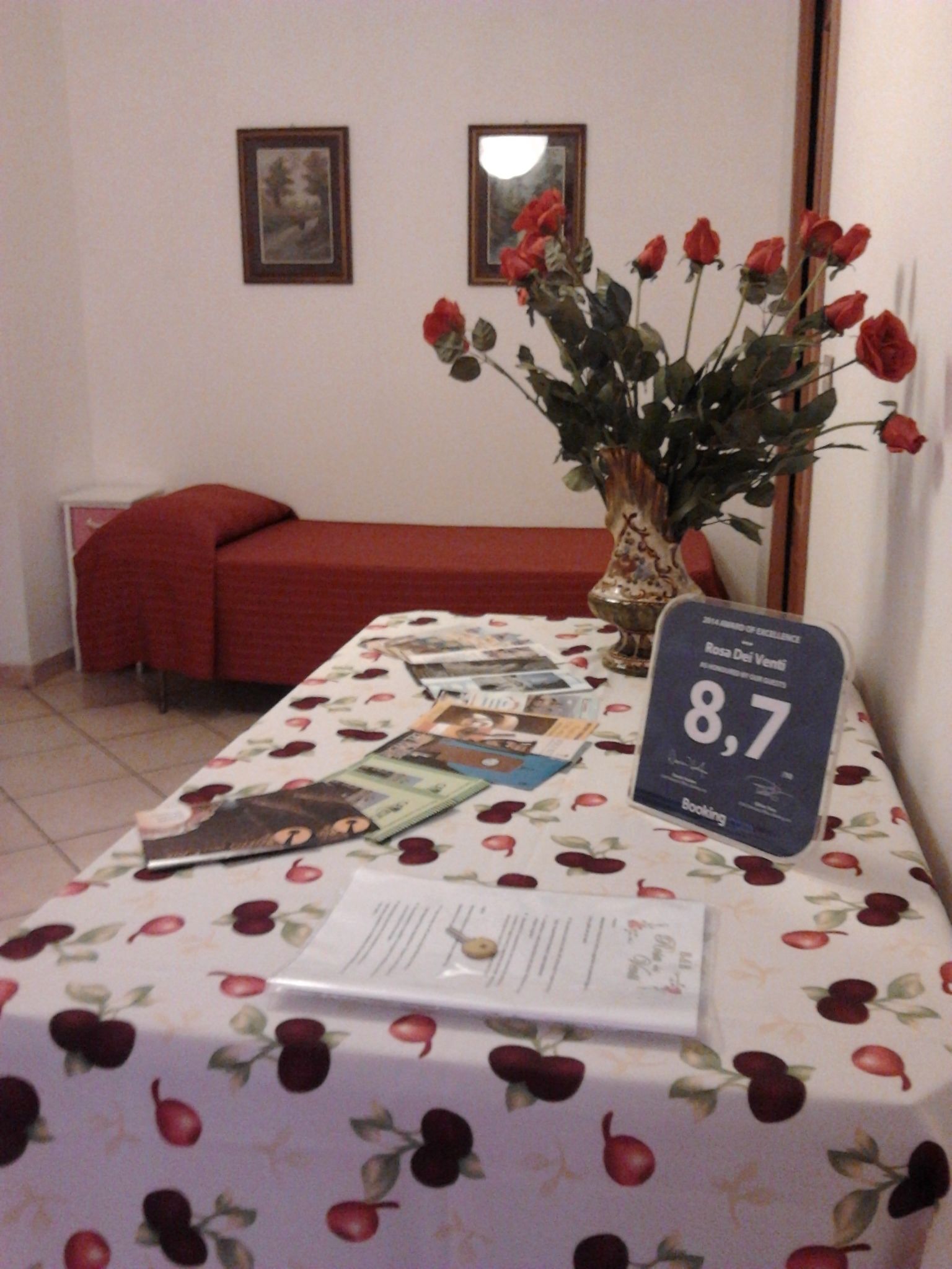 Habitación de hotel con una mesa dispuesta para una comida, un jarrón con rosas rojas y un cartel que indica una tarifa de habitación de 8,7.