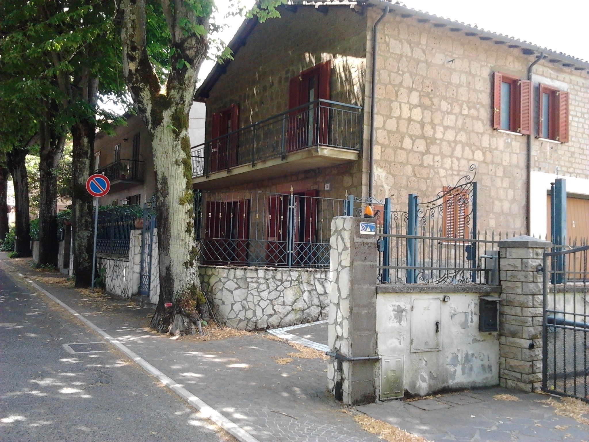 A two-story stone building with a balcony, a no parking sign, and a gated entrance.