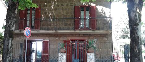 A two-story building with a stone facade, red shutters, and a metal gate.