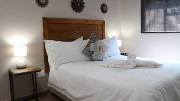 Una cama bien tendida con sábanas blancas, cabecera de madera y almohadones decorativos.