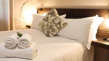 Una cama bien hecha con sábanas blancas, un cojín floral y toallas enrolladas al lado.