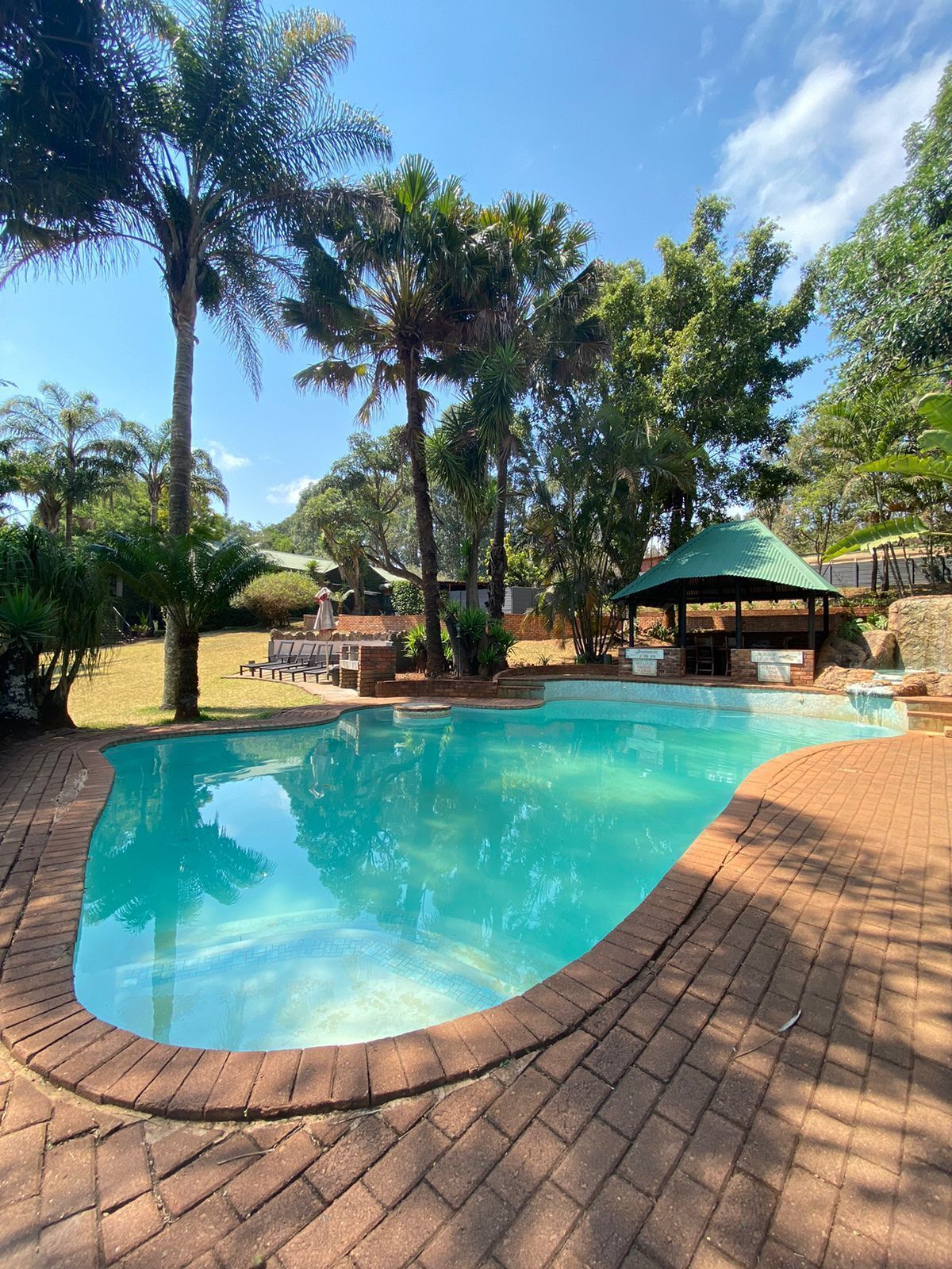 A swimming pool with a brick deck, surrounded by palm trees and a gazebo.