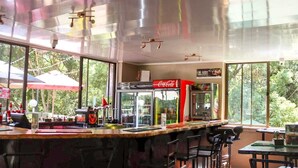 A restaurant with a bar area, seating, and large windows offering a view of the outdoors. - The Ultimate Lodge (Louis Trichardt)