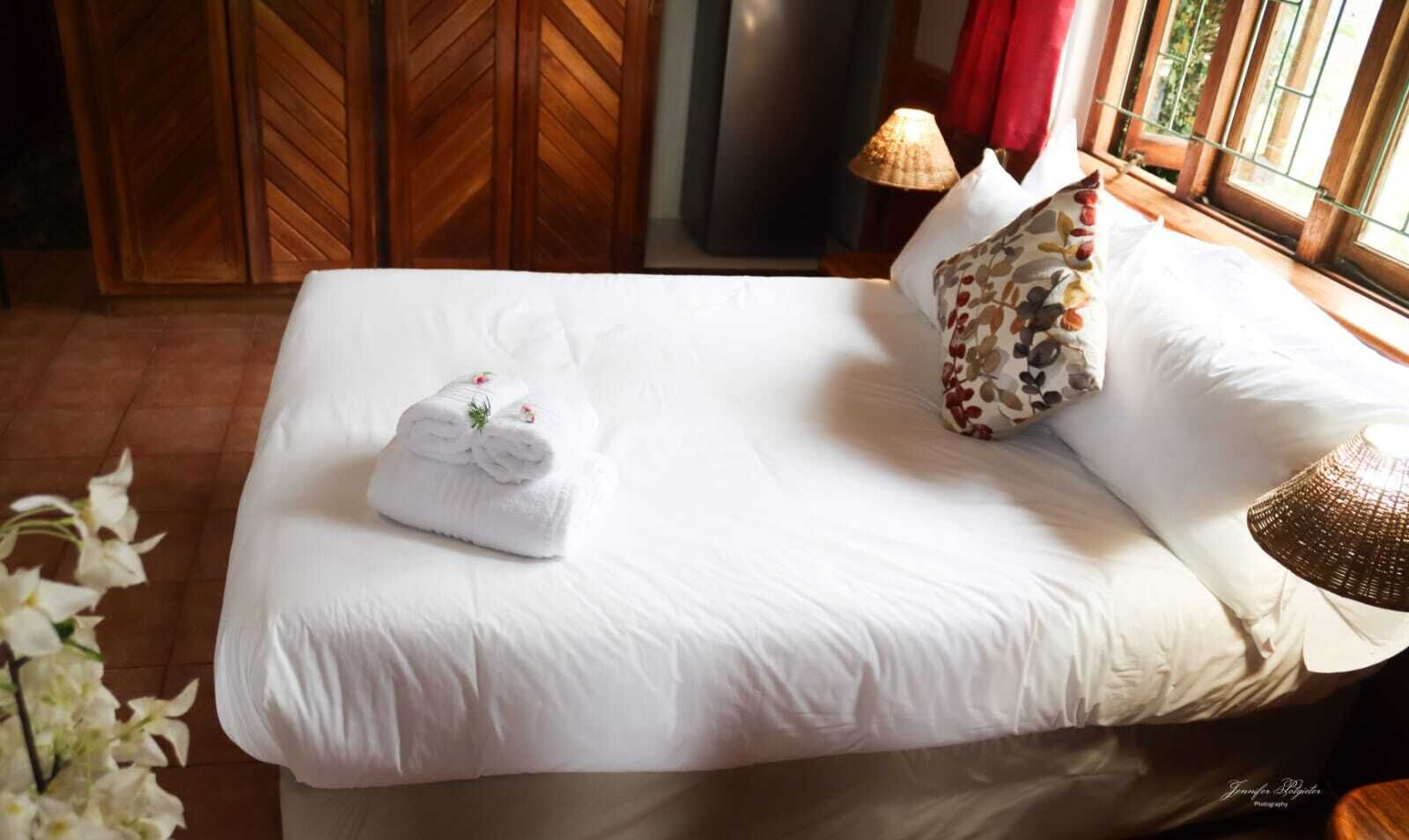A neatly made bed with white linens, a floral pillow, and a rolled towel on the side.