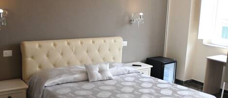 A bedroom with a tufted headboard, a large bed with a patterned bedspread, a bedside table, a nightstand, a desk, a chair, and a chandelier.