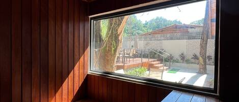 A room with wooden slatted walls and a large window overlooking a patio area with outdoor furniture.